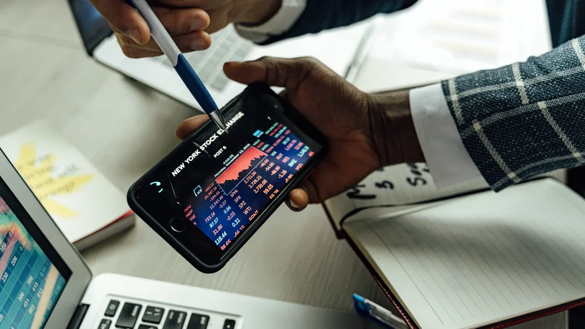 Hands pointing at a phone with trading chart