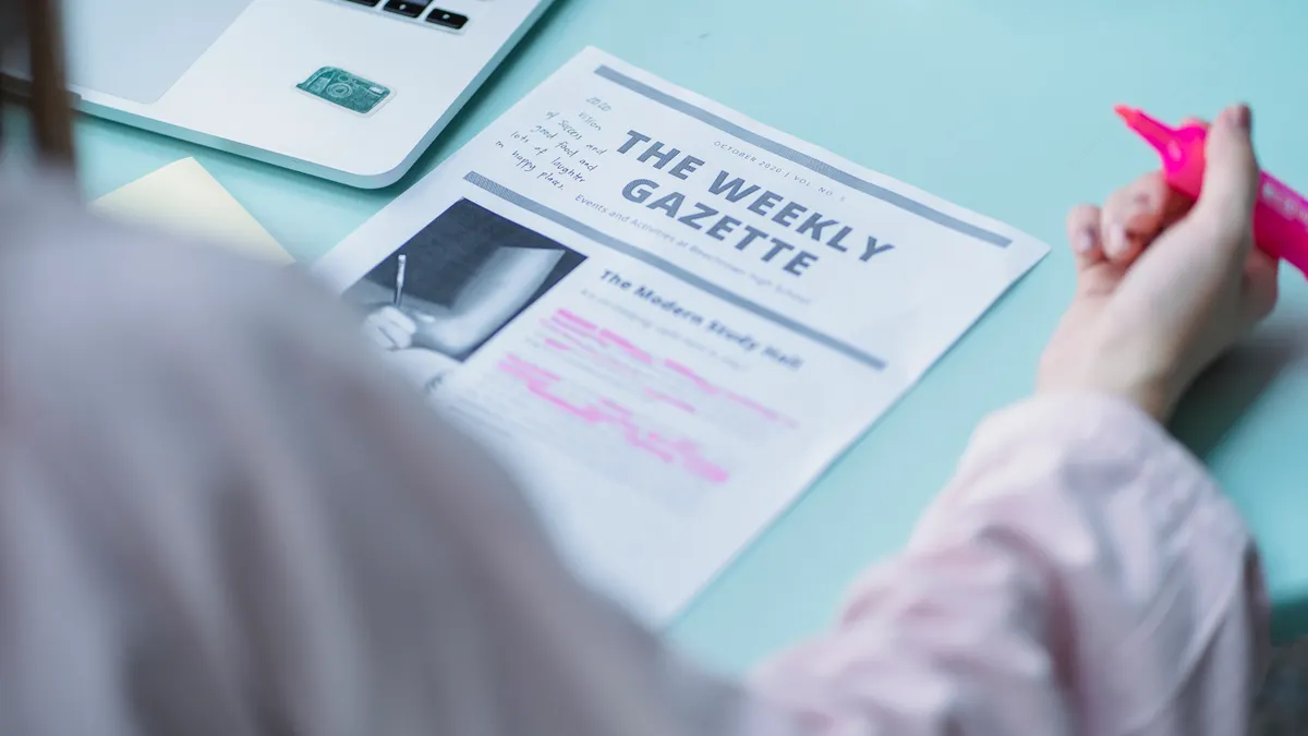 Person annotating a printed newsletter next to a laptop